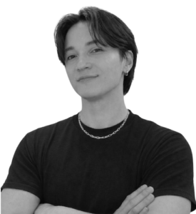Portrait of a person with short dark hair, wearing a black T-shirt and a silver chain, arms crossed and looking at the camera.