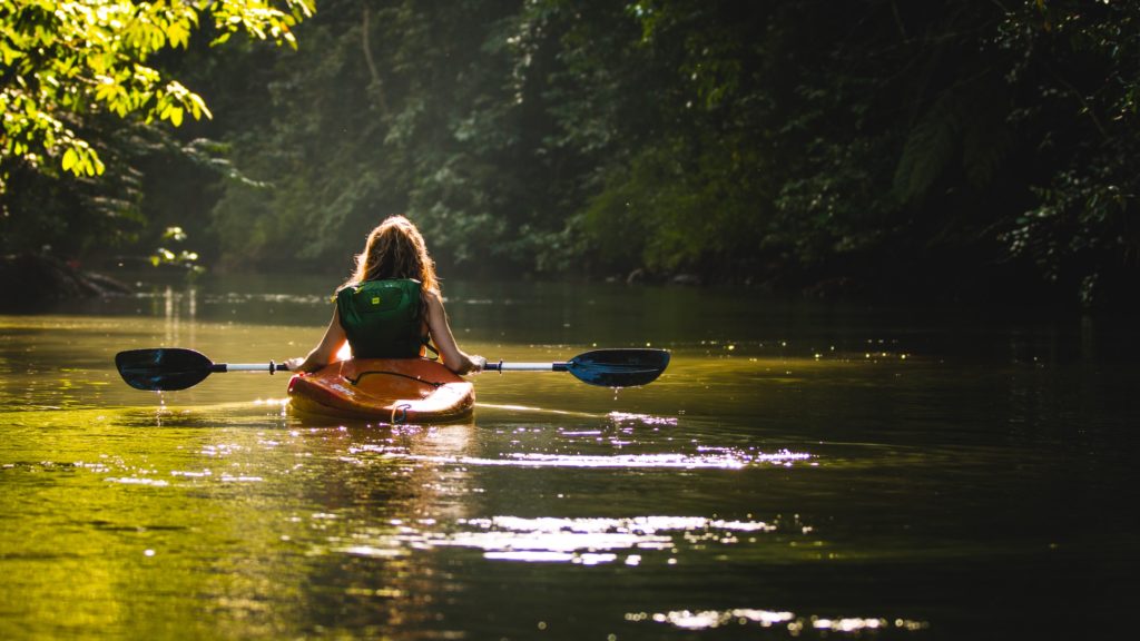 Woman kayaking on a river with a lush riverbank
