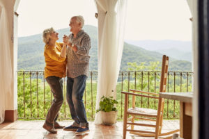 Loving senior couple dancing in balcony. Happy man and woman are spending leisure time together. They are at home.