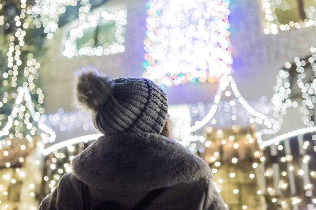 Rear view of fashionable female enjoying christmas spirit in front of house with beautiful holiday decoration.