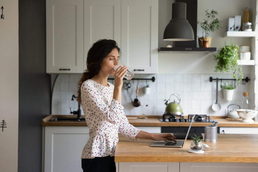 Woman work on laptop drinking water at home