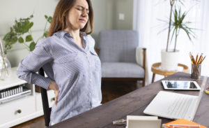 Freelancer young woman suffering with back pain while working in her office at home